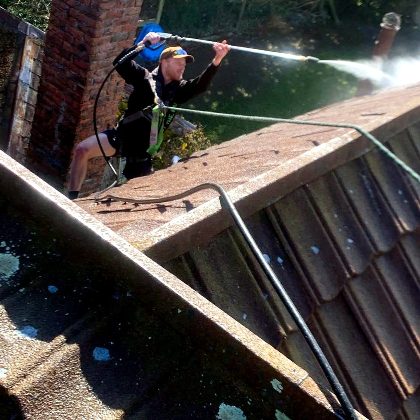 Roofer in a harness pressure-washing a tile roof